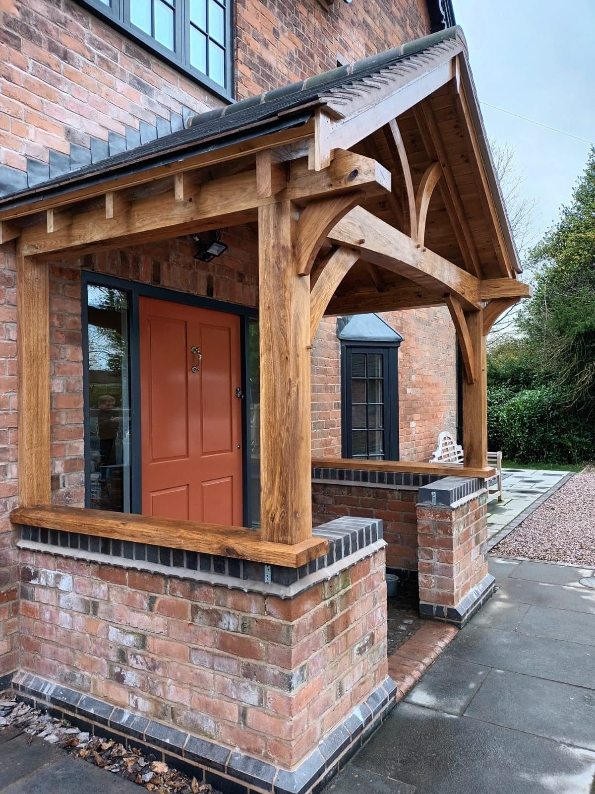 A one-off oak porch on a brick house — deep frame with curved braces, oak sill beams and a corner return over brick dwarf walls