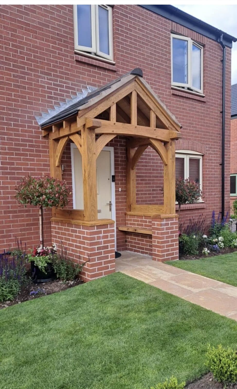 A one-off oak porch on a new-build home, oak posts on brick dwarf walls with a built-in bench and a sandstone path