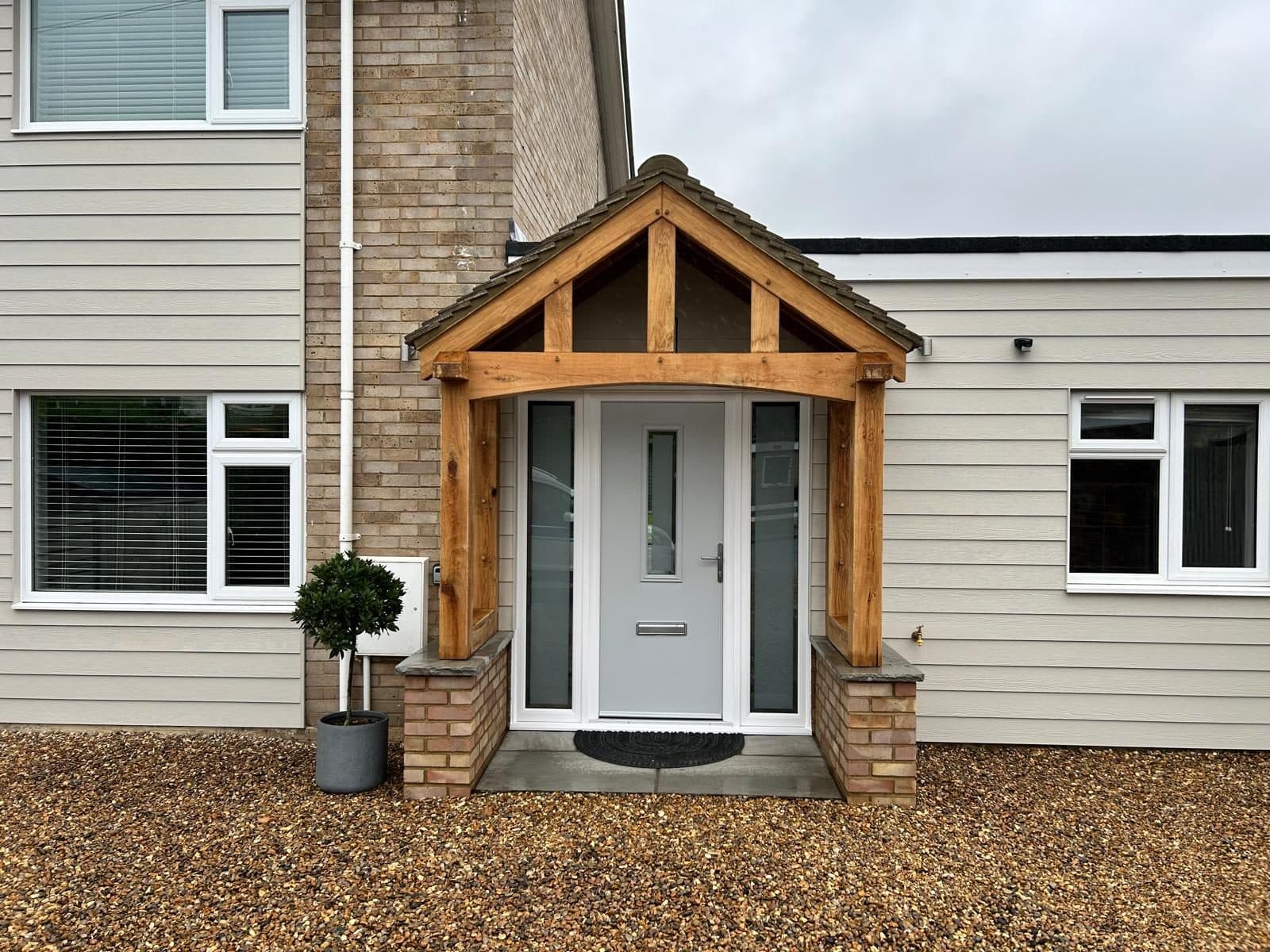 The Broadway oak porch on a cream-clad house, oak posts on brick plinths sheltering a pale grey front door