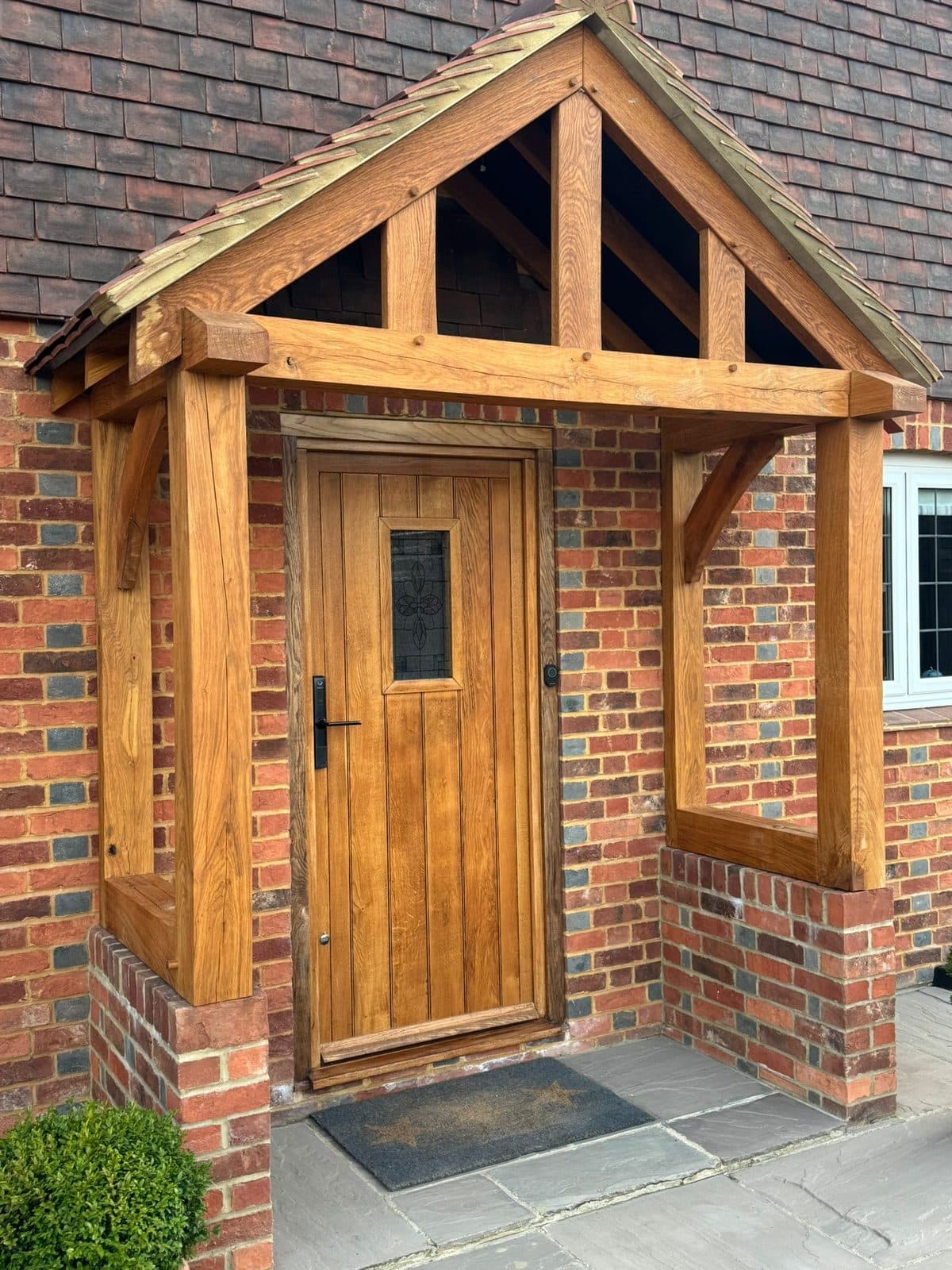 The Hartlebury oak porch on a brick home — open gable over an oak front door, on brick dwarf walls with a sandstone floor
