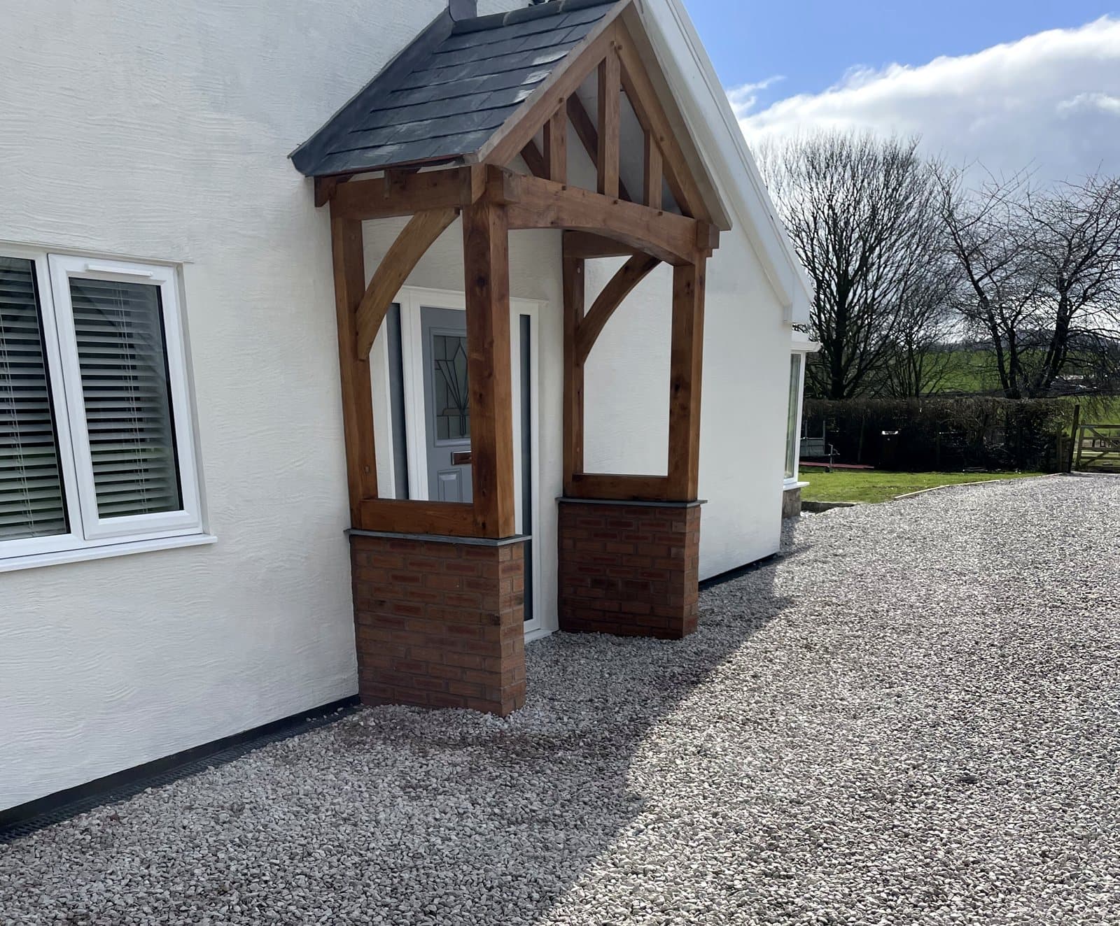 The Malvern oak porch on a white rendered house, slate roof and brick plinths matching the property