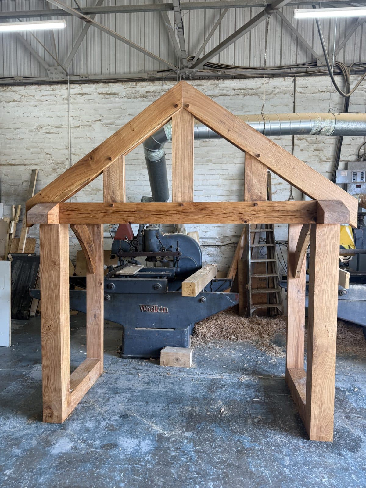 Front elevation of an oak porch frame standing square on the workshop floor, gable uprights and braces pegged home