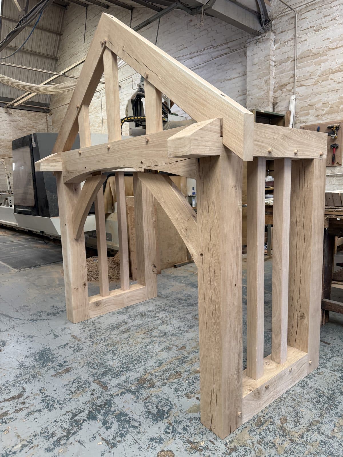 An oak porch frame dry-fitted on the workshop floor, curved braces and side screens pegged, ready to be taken apart