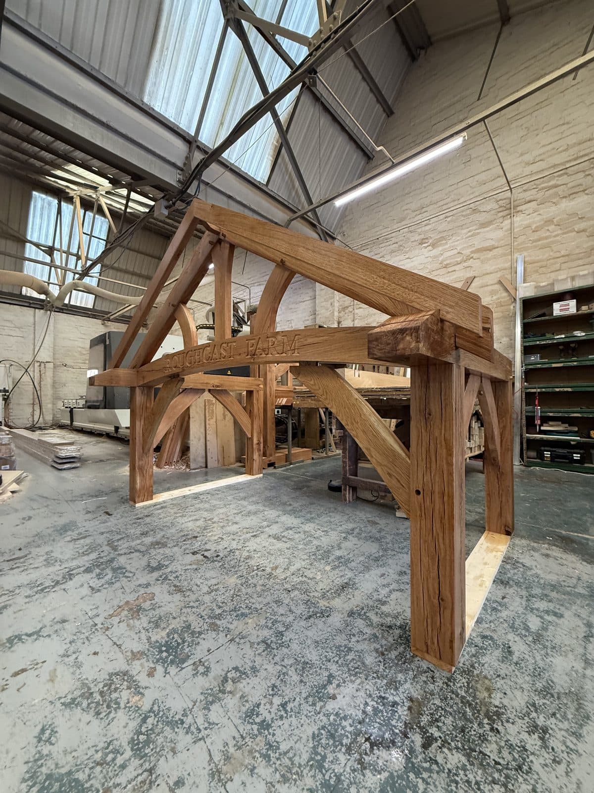 An oiled oak porch frame standing complete in the workshop, ROUGHCAST FARM carved along its curved beam